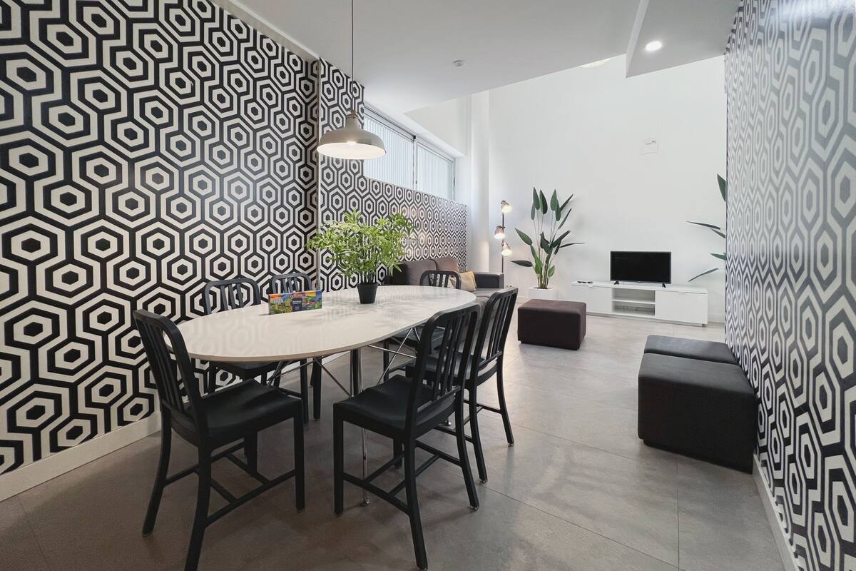 Un comedor moderno con un muro de diseño geométrico, una mesa redonda, sillas negras y una planta en maceta.