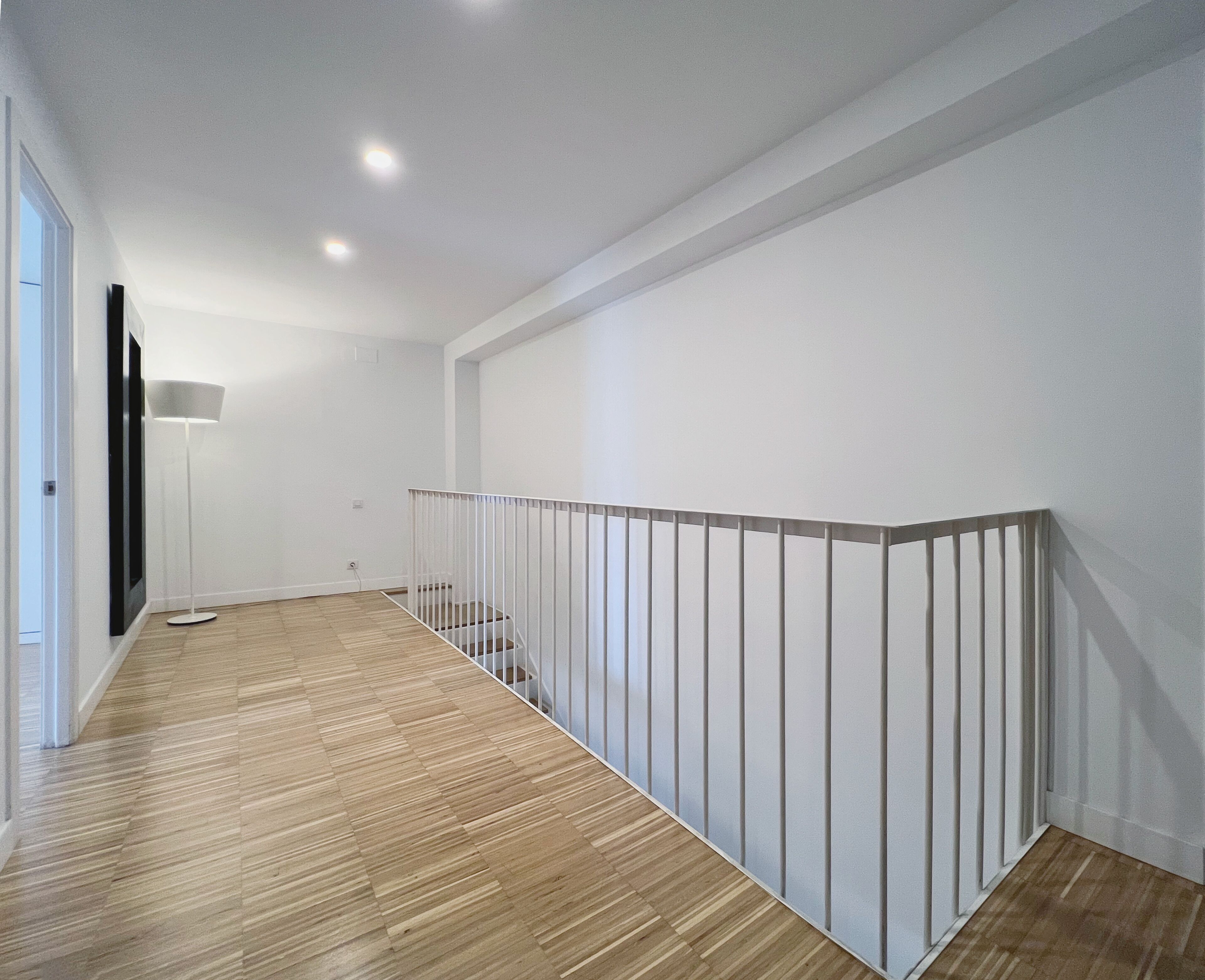 Ein modernes Interieur mit Holzboden, weißen Wänden und einem weißen Geländer.