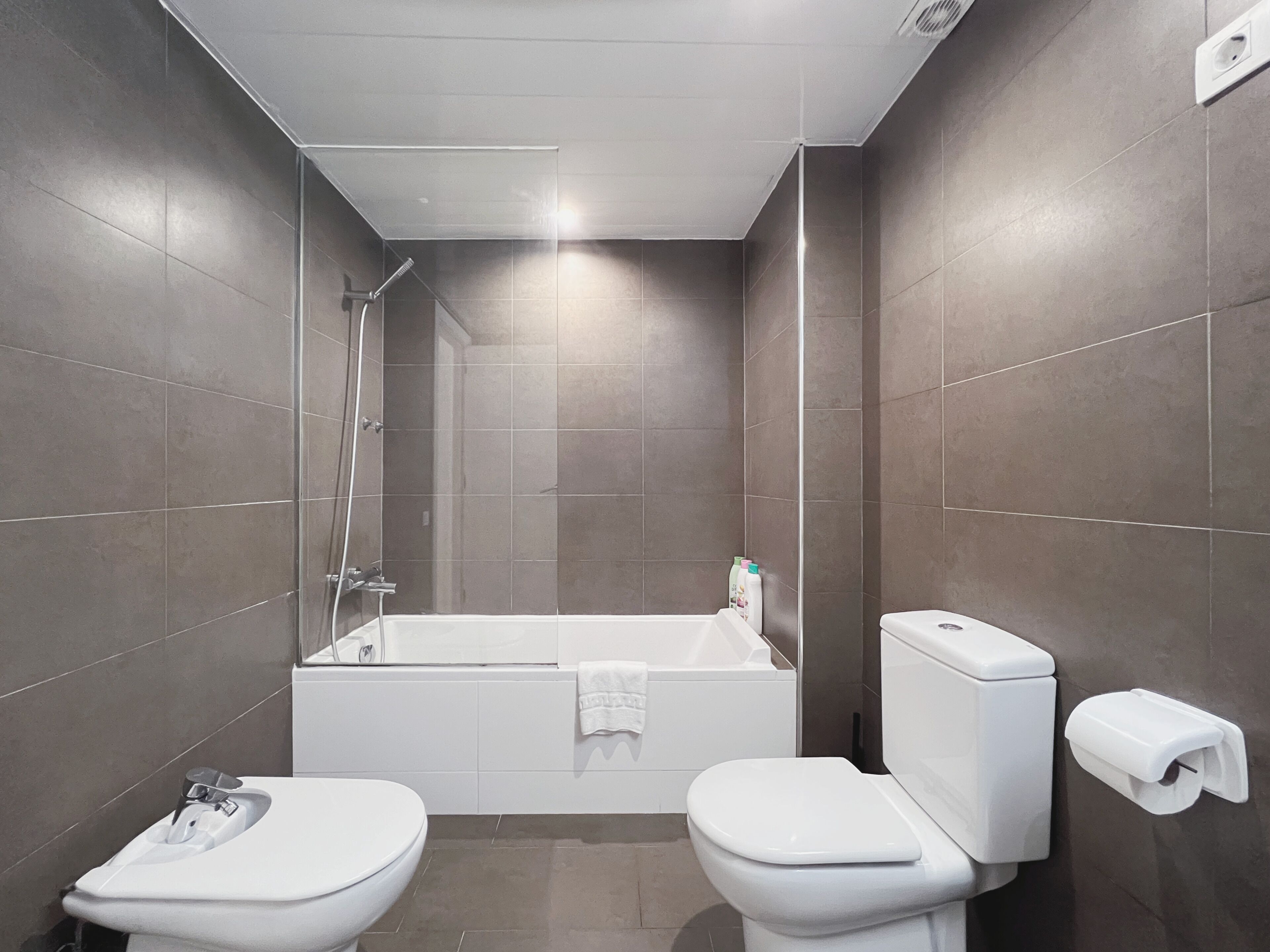 A modern bathroom with a bathtub, two toilets, and a shower.