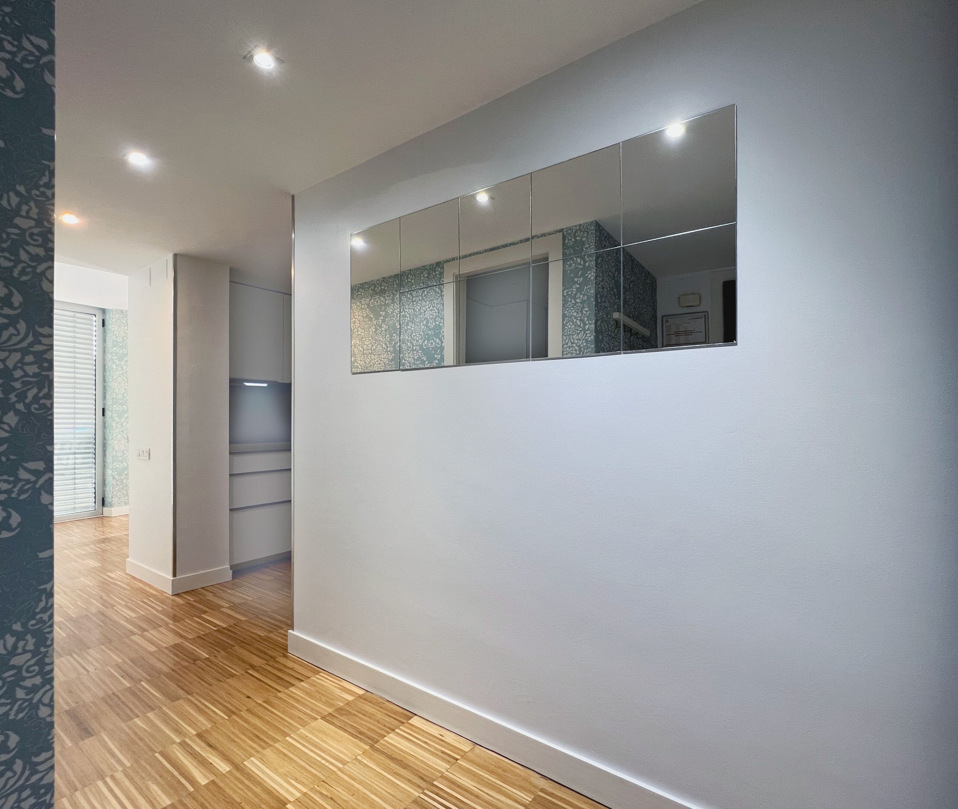 Un couloir doté d’un plancher en bois, d’un mur recouvert de miroirs et de spots encastrés au plafond.