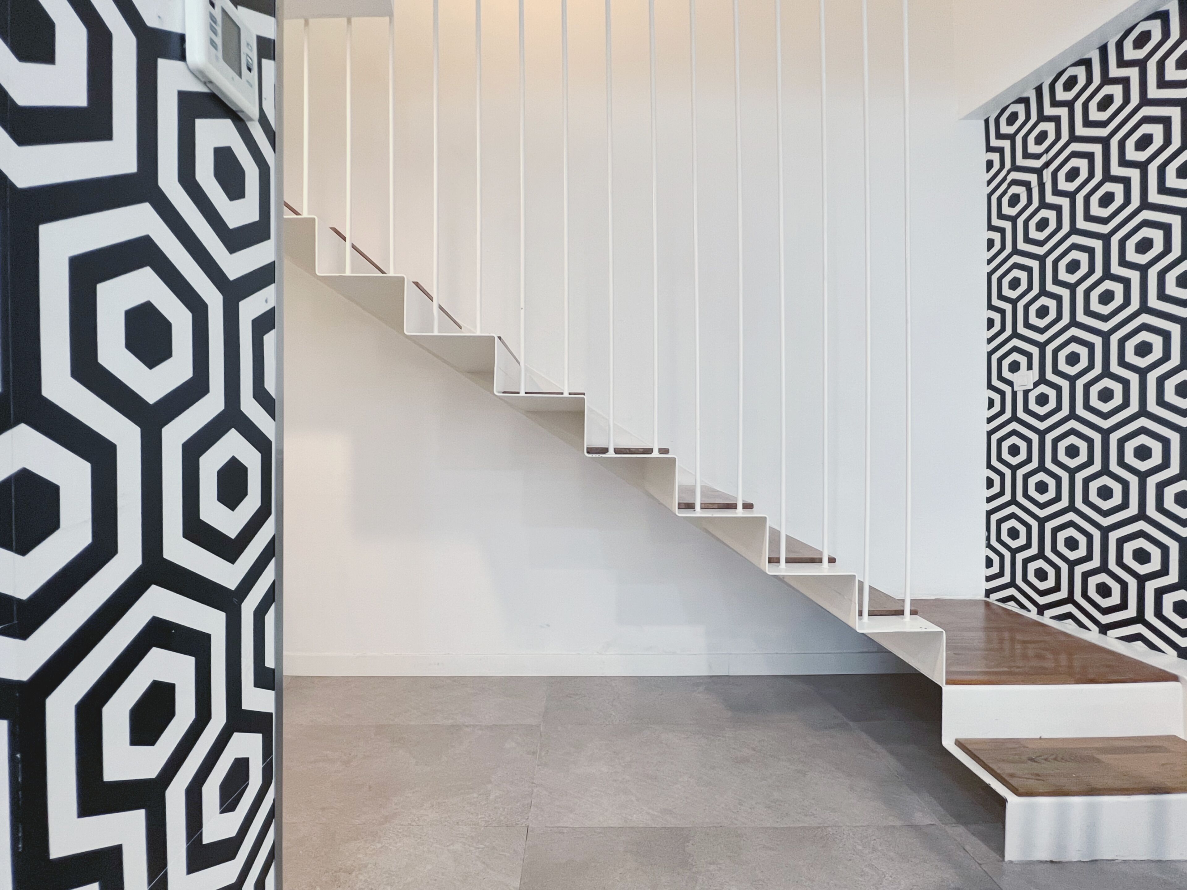 A staircase with white railings and a geometric patterned wall to the right.