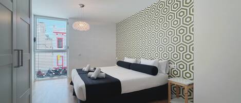 A modern bedroom with a bed, a nightstand, a patterned wall, and a window with a view of the street.