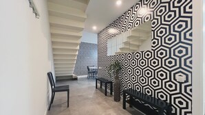Un interior moderno con un muro de patrón geométrico, una escalera y una zona de estar con un banco y sillas.