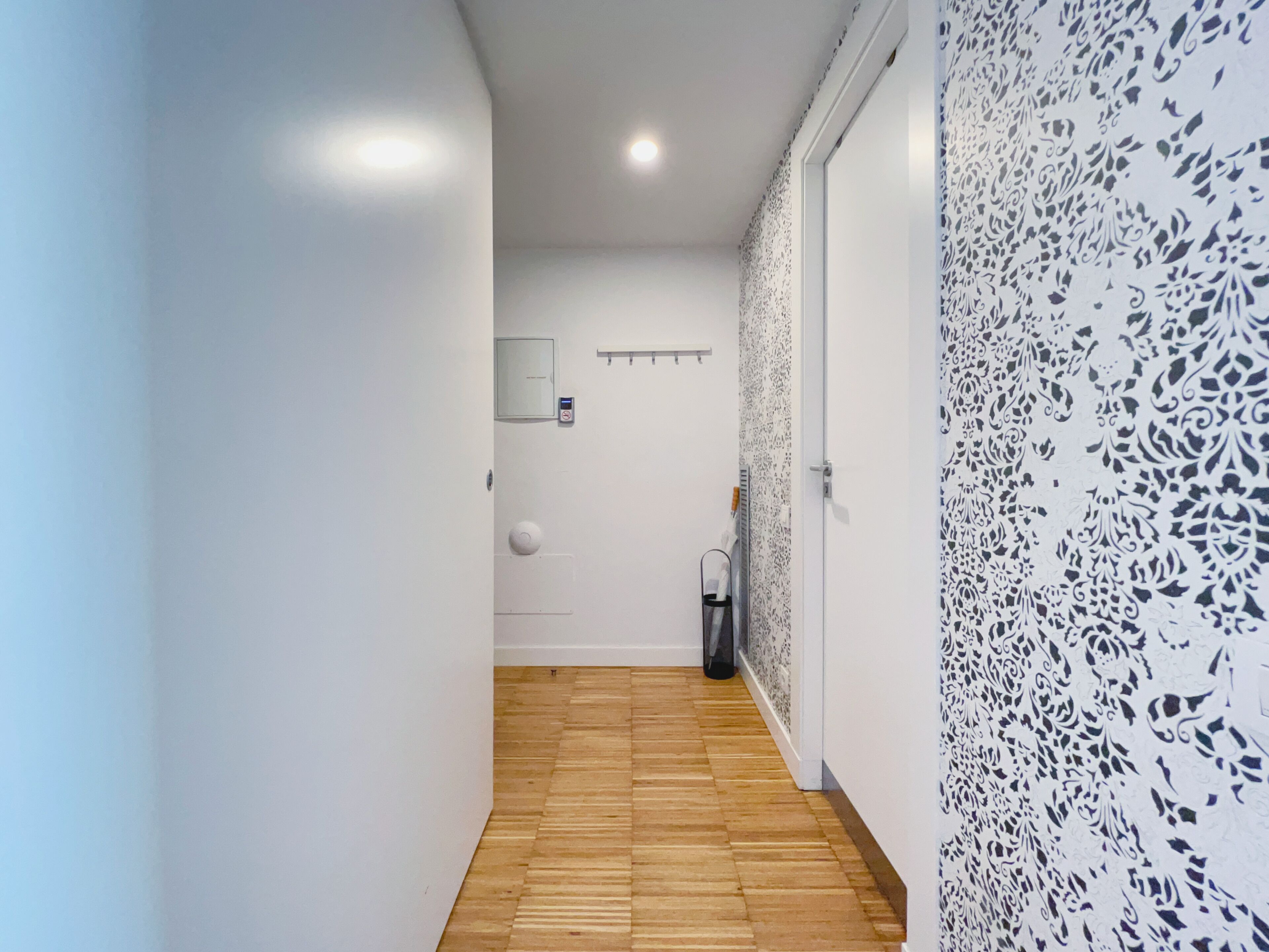 Un pasillo con suelo de madera, paredes blancas y un diseño decorativo en la pared derecha.