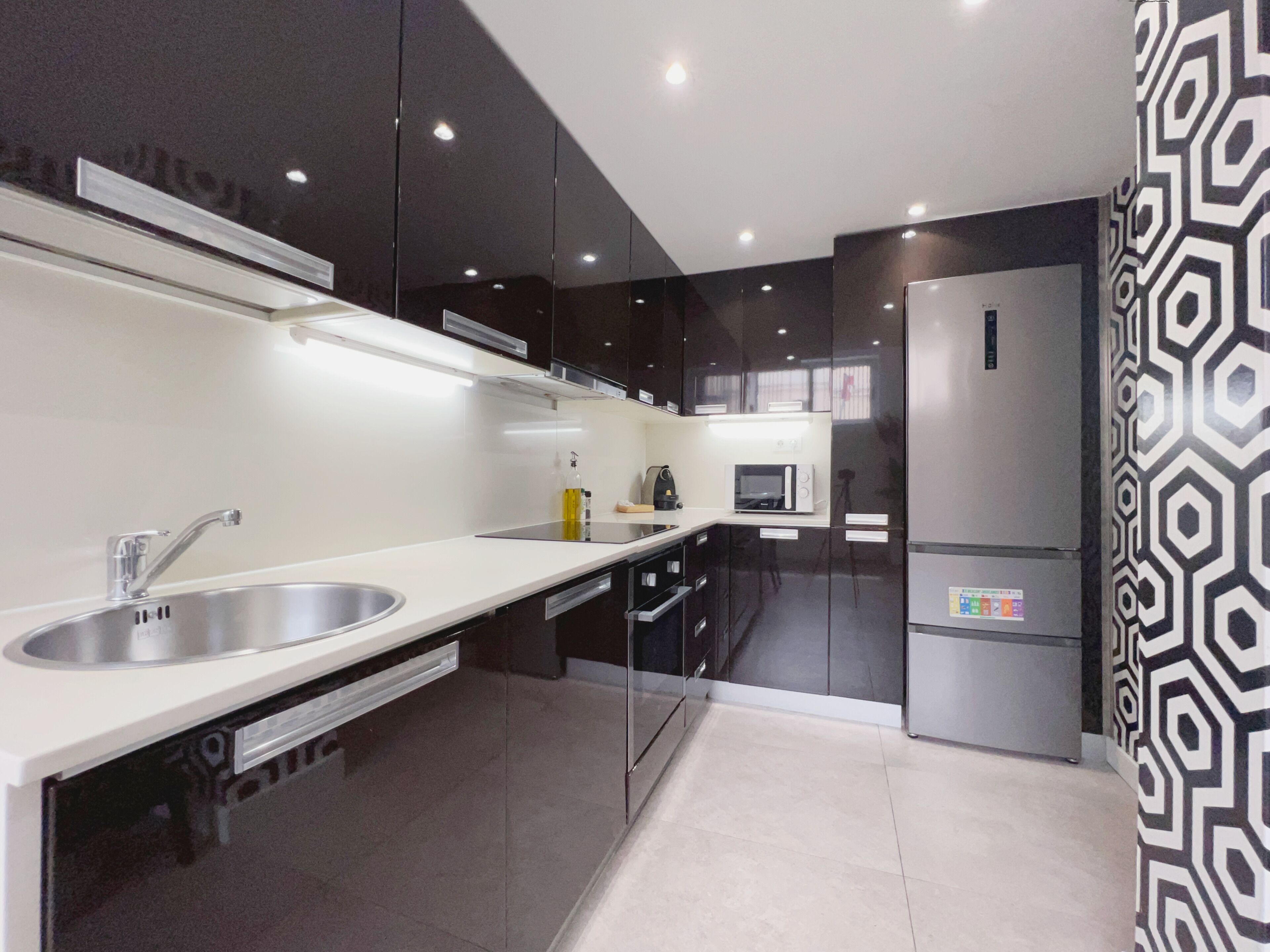 Una cocina moderna con un lavamanos de acero inoxidable, gabinetes negros, un microondas y un refrigerador.
