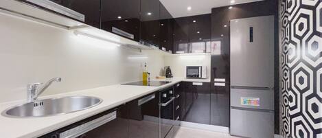 Una cocina moderna con un lavamanos de acero inoxidable, gabinetes negros, un microondas y un refrigerador.