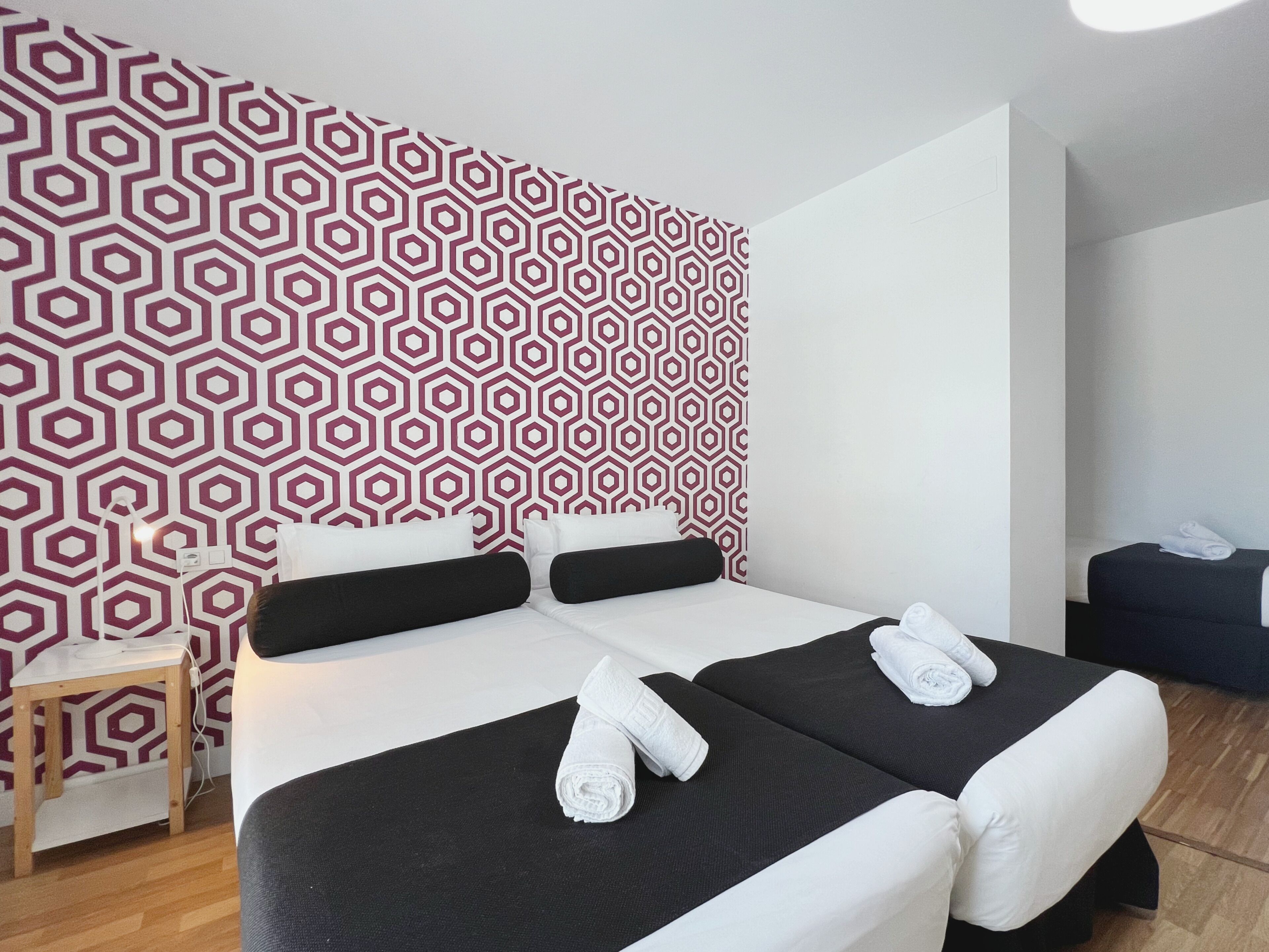 Una habitación de hotel con pared de diseño geométrico, una cama con ropa de cama blanco y negro, y una pequeña mesa de madera.