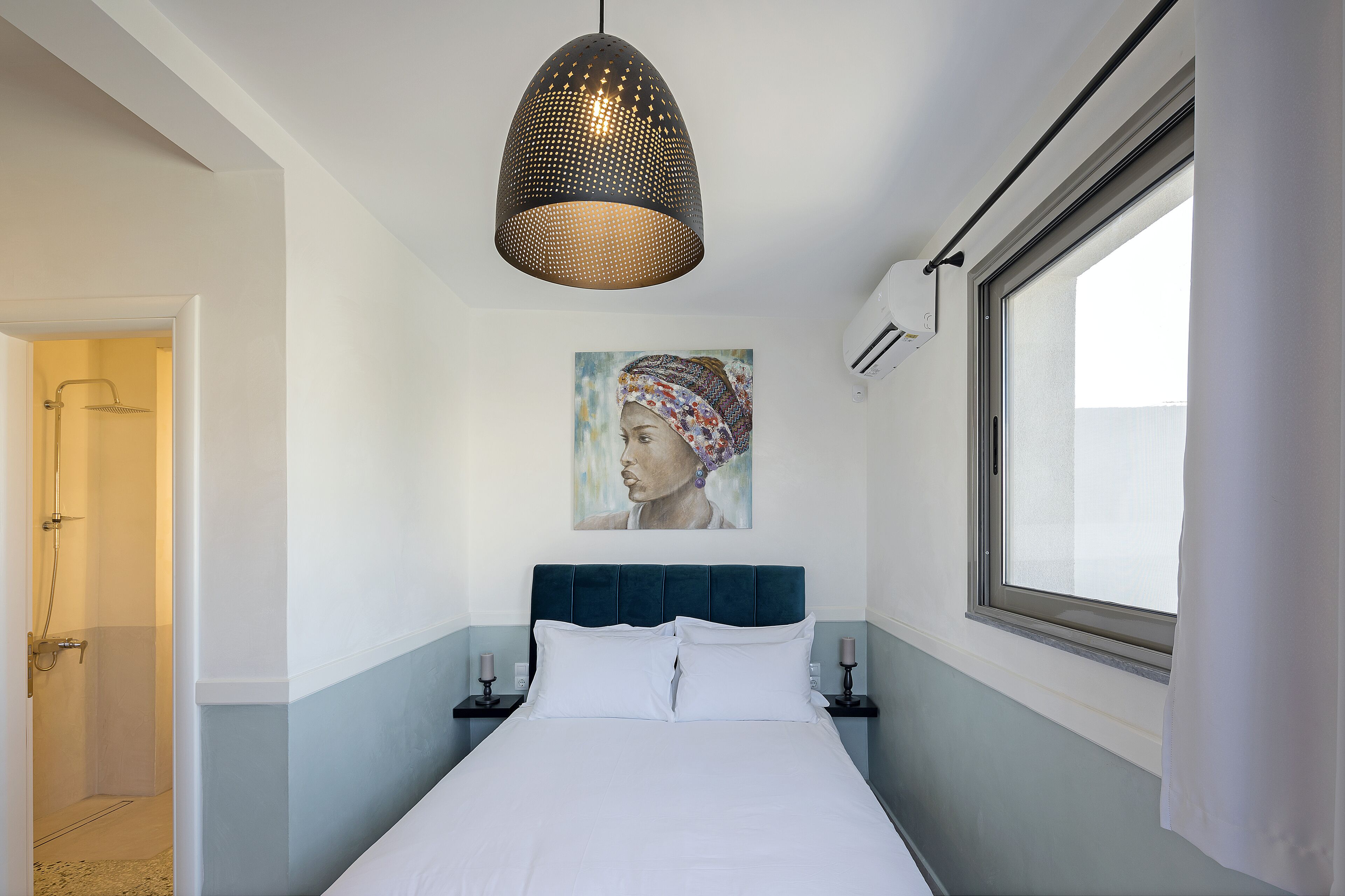 A bedroom with a bed, a window, a painting, and a pendant light.