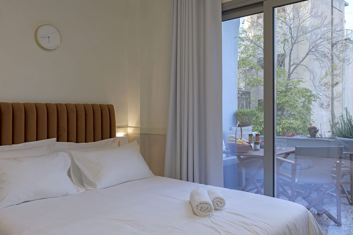 A hotel room with a bed, pillows, a headboard, a window with curtains, and a view of the outside.