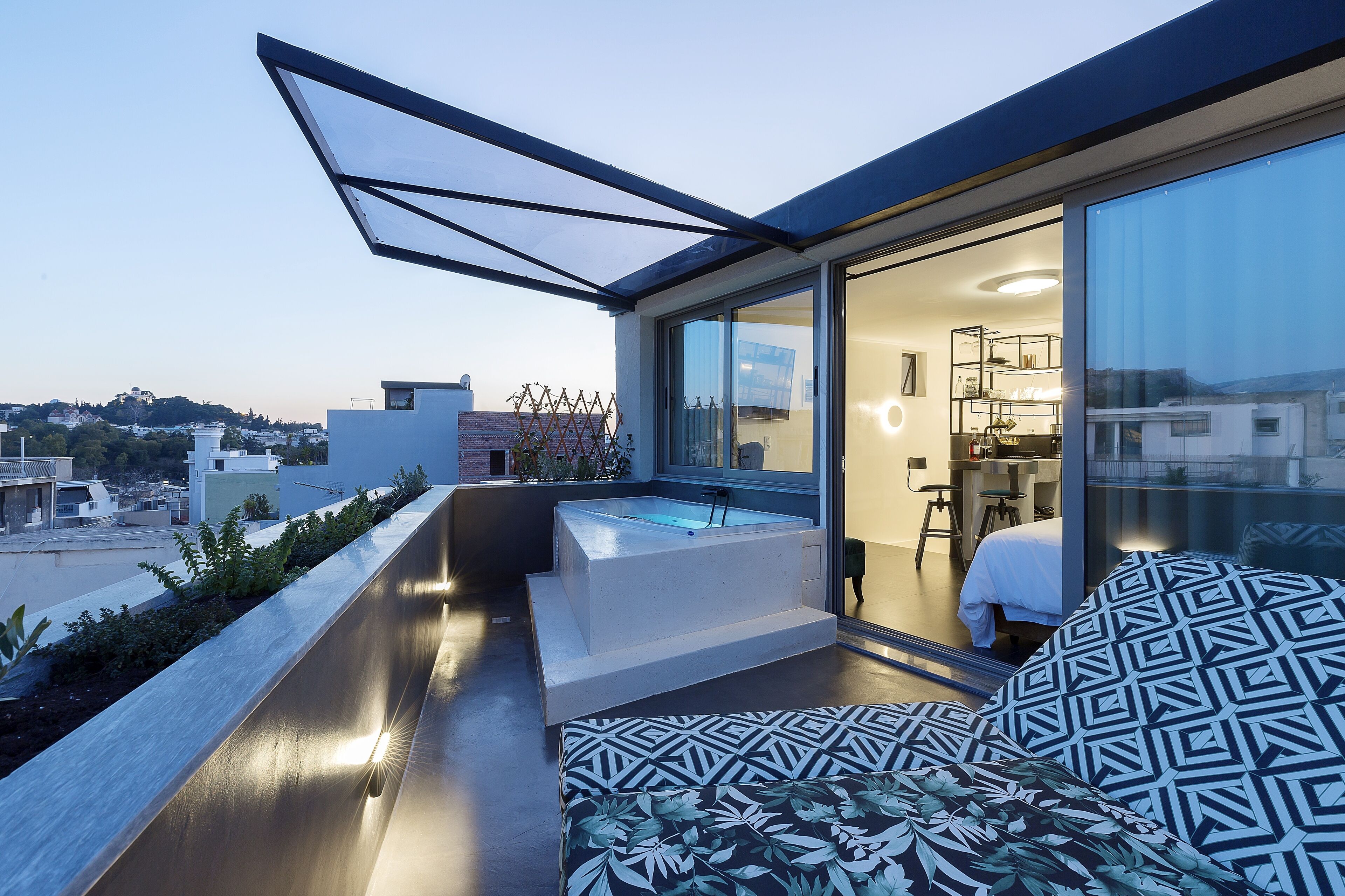 A modern rooftop terrace with a hot tub, a glass-enclosed room, and a patterned sofa.