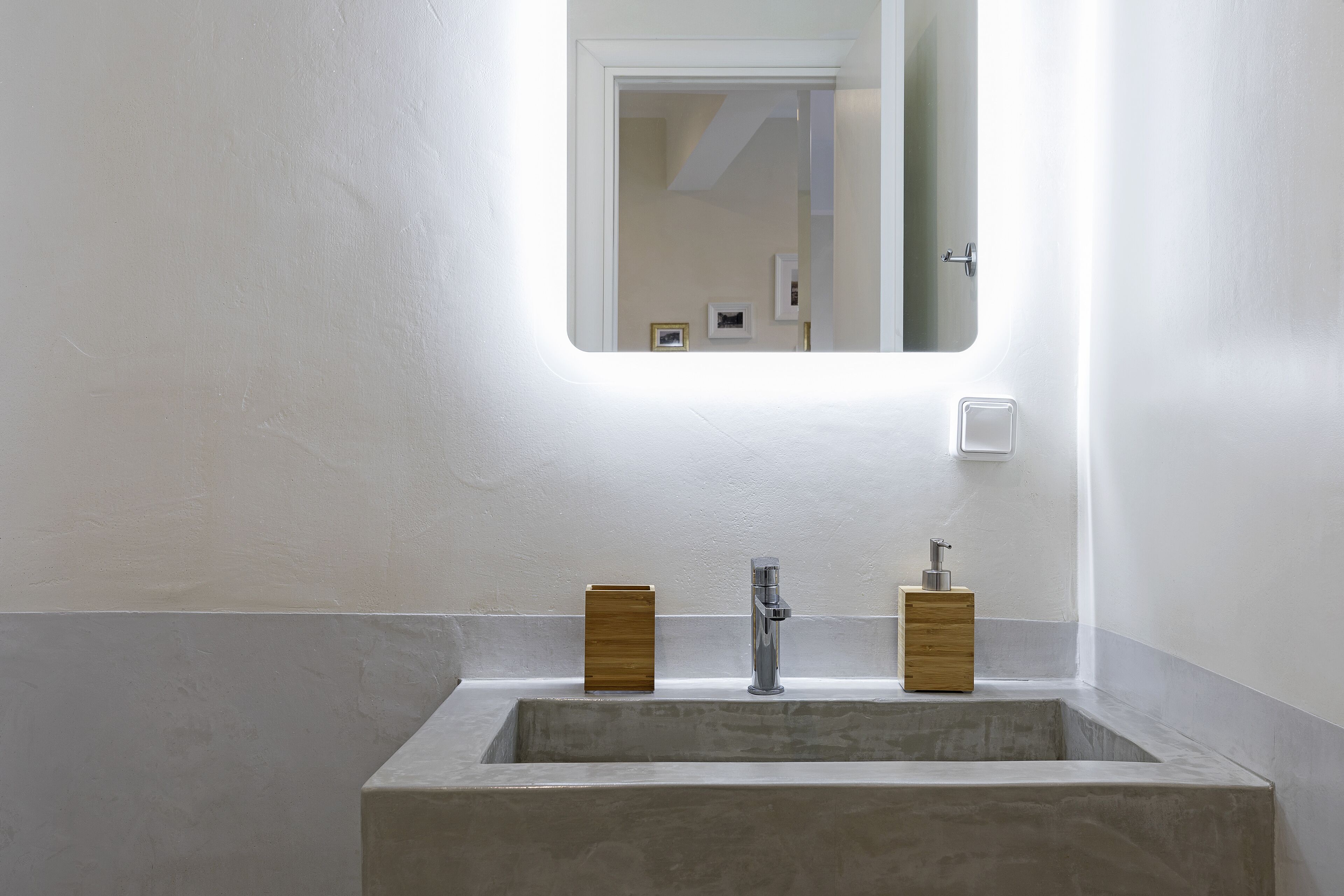 Une salle de bain avec un lavabo rectangulaire, un miroir au-dessus, et deux distributeurs de savon en bois.