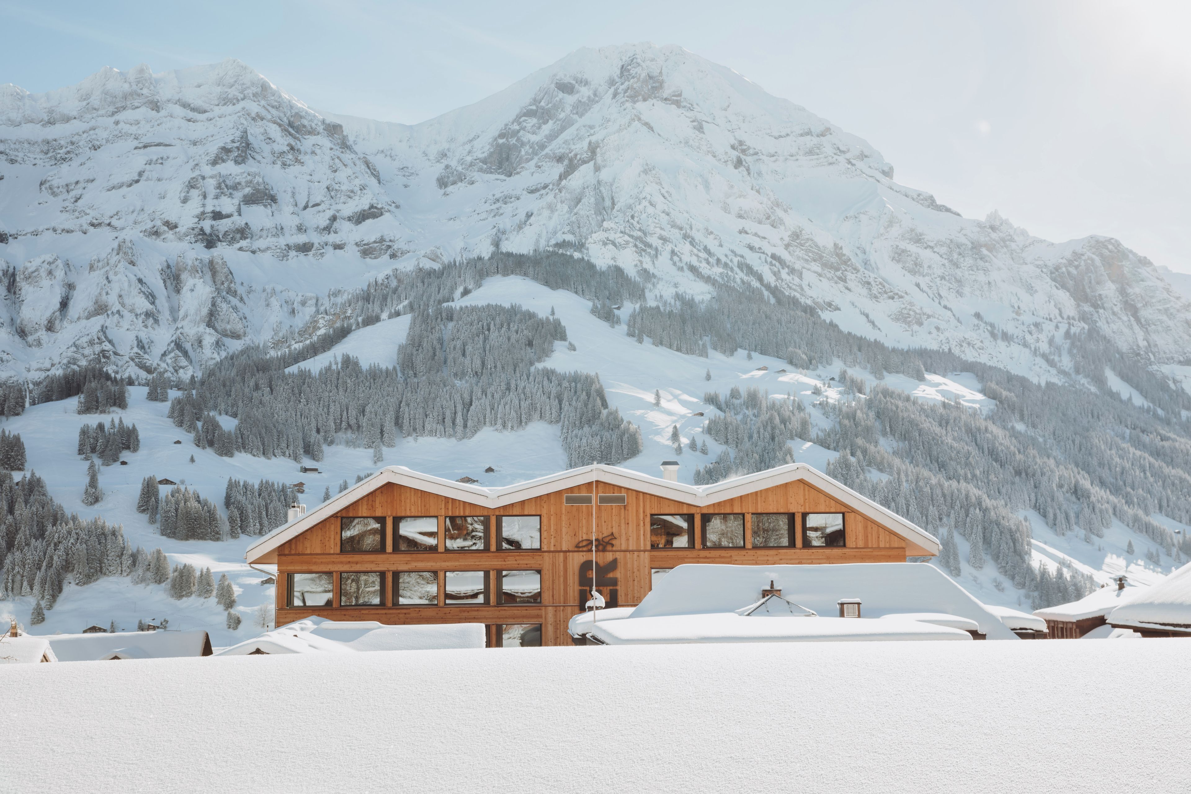 A wooden chalet with multiple windows, set against a backdrop of snow-covered mountains.