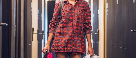 A person walking down a corridor with doors on both sides, holding a pink bag and white sneakers.