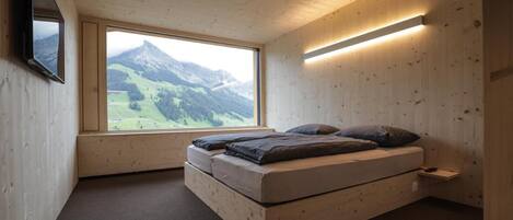 Une chambre à coucher avec un lit, un téléviseur fixé au mur et une fenêtre donnant sur la montagne.