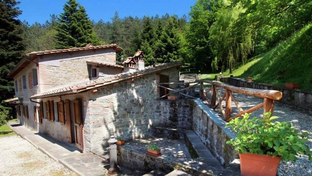 A stone building with a rustic exterior, a wooden staircase leading to a bridge over a water channel, and a potted plant on the right. - Locanda Le Isole - "Mountain Hut" Apartment (last) (scarperia)
