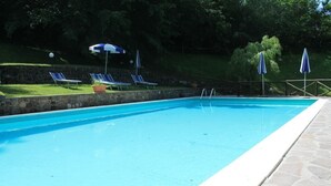 A rectangular swimming pool with a stone border, surrounded by a stone deck. There are lounge chairs and umbrellas in the background. - Locanda Le Isole - "Mountain Hut" Apartment (last) (scarperia)