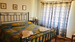 A bedroom with a metal bed frame, a colorful quilt, and a floral curtain. - Locanda Le Isole - "Mountain Hut" Apartment (last) (scarperia)