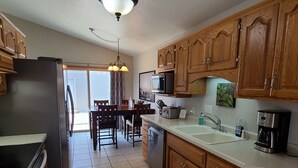 A kitchen with wooden cabinets, a refrigerator, a microwave, a coffee maker, and a dining area with a table and chairs. - Convenient to Green Bay's beltline where you can get anywhere in 15 minutes. (Green Bay)