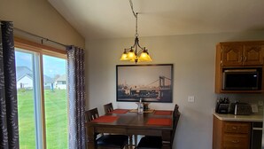 A dining area with a table and chairs, a chandelier, a kitchen with cabinets and appliances, and a large window with curtains. - Convenient to Green Bay's beltline where you can get anywhere in 15 minutes. (Green Bay)