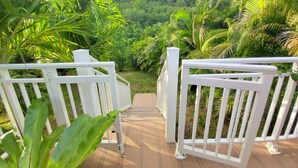 A wooden deck with white railings overlooking a lush, green landscape with palm trees and a hill in the background. - Nature Paradise Cottage • Lovers' Stay (Le Diamant)