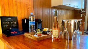 A wooden bar area with a Nespresso machine, water bottles, a wine bottle, and a glass decanter. - Nature Paradise Cottage • Lovers' Stay (Le Diamant)