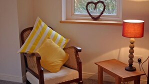 A wooden chair with yellow and white striped pillows, a small wooden table with a lamp, and a heart-shaped decoration on a windowsill. - Great location to explore Connemara (Connemara)