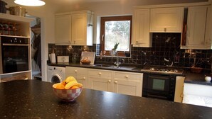 A kitchen with white cabinets, a black countertop, a sink, a stove, and a window. - Great location to explore Connemara (Connemara)