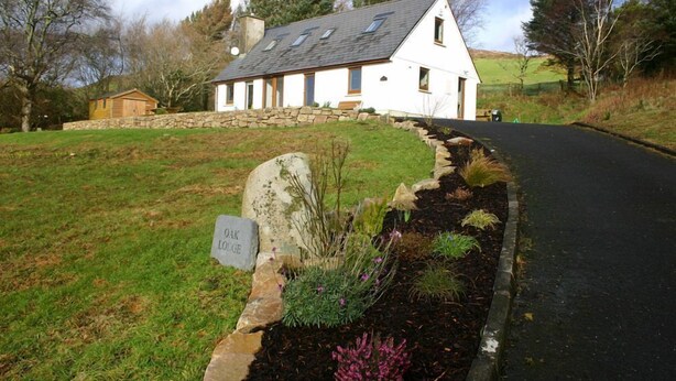 A white house with a stone wall and a garden with various plants and a sign that reads "OK LODGE". - Great location to explore Connemara (Connemara)