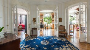 Ruime kamer met een groot blauw tapijt met patroon, houten meubels en uitzicht op een eetgedeelte met een rode bank.