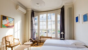 Een hotelkamer met twee bedden, een houten stoel, een tafeltje en een raam met gordijnen.