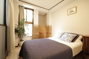 A bedroom with a bed, a potted plant, a window, and a wooden wardrobe.