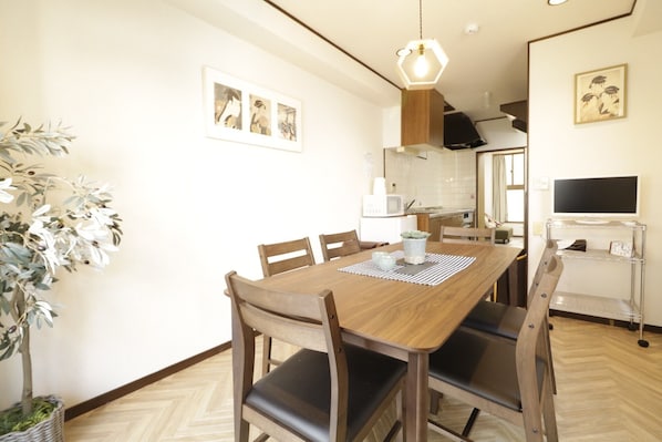 A dining area with a wooden table, chairs, a hanging light fixture, and a potted plant.