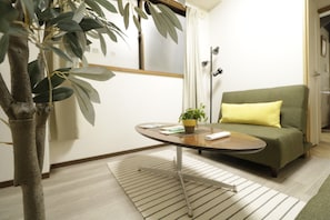 A room with a green sofa, a small table with a plant, and a potted plant in the corner.