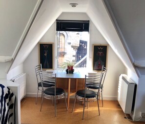 Un coin repas comprenant une table et des chaises, un radiateur et une fenêtre avec des stores.