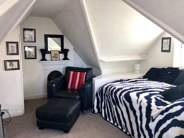 Une petite chambre mansardée, chaleureuse et accueillante, avec un fauteuil en cuir noir, un lit à motifs zébrés et une cheminée.