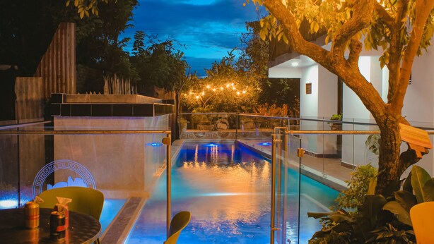An indoor swimming pool with a glass barrier, surrounded by plants and trees, and a view of the sky at dusk. - Hospedería Sol Del Desierto - Hostel (Villavieja)