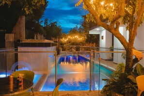 An indoor swimming pool with a glass barrier, surrounded by plants and trees, and a view of the sky at dusk. - Hospedería Sol Del Desierto - Hostel (Villavieja)