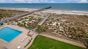 A beachside hotel with a swimming pool, lounge chairs, and a pier extending into the ocean.