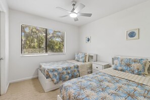Quarto com duas camas, um ventilador de teto, uma janela com persianas e duas mesas de cabeceira.