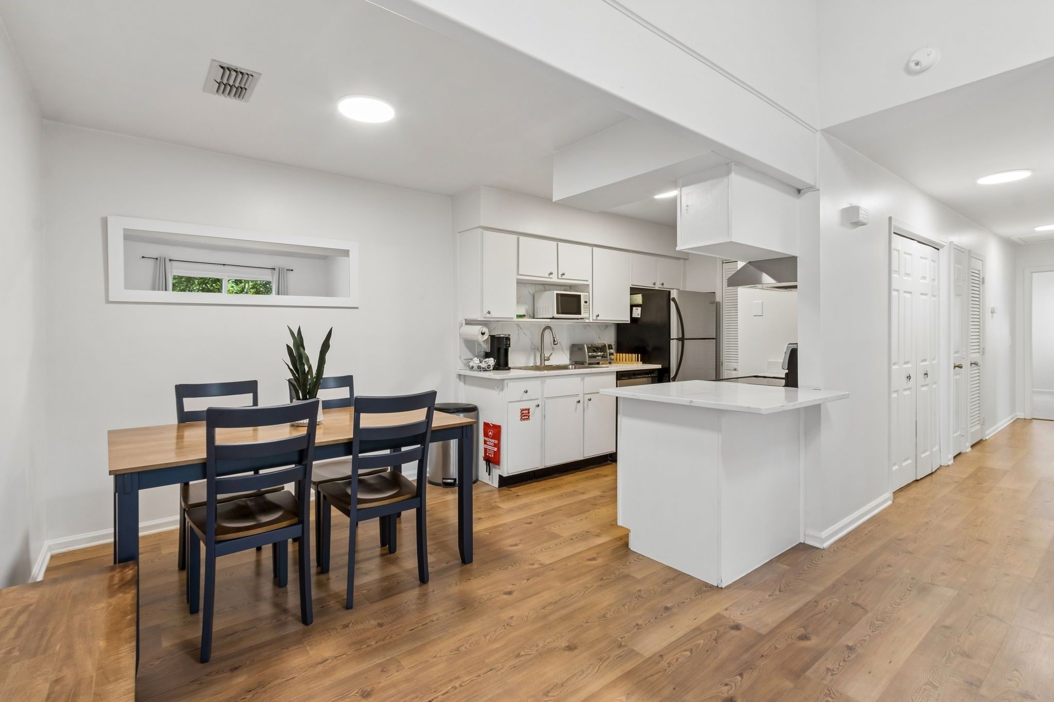 A modern kitchen with white cabinetry, a central island, and a dining area with a table and chairs.