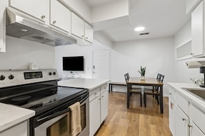 A modern kitchen with white cabinetry, a black stove, and a dining area with a wooden table and chairs.