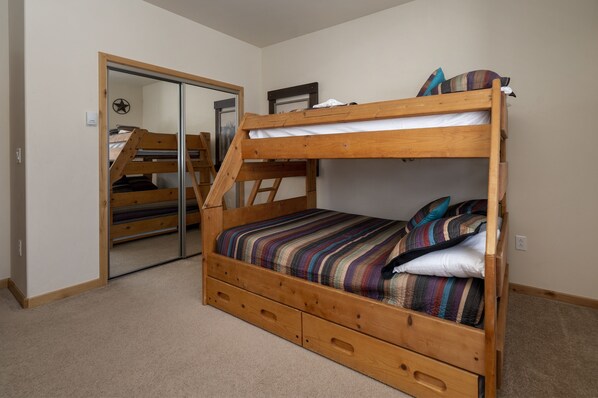 A bunk bed with a wooden frame, a mirror, and a door leading to another room.