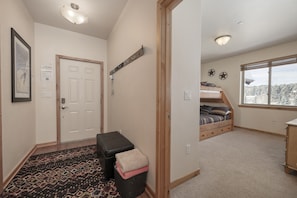 A room with a bunk bed, a small desk, a window with a view, and a door with a light switch. - Trailhead Lodge 734 2 Bedroom Condo by RedAwning (Winter Park)