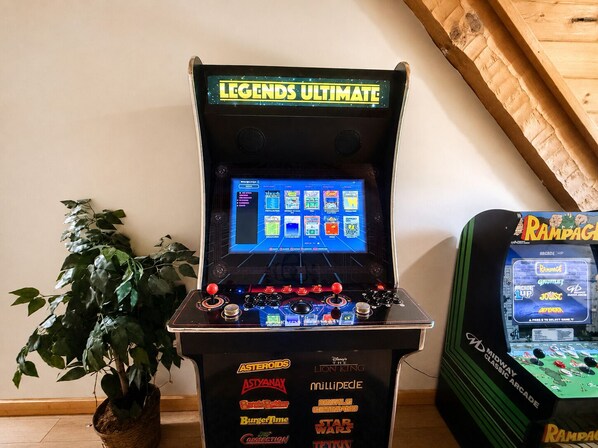 Una máquina de arcade retro con una selección de juegos, incluyendo Asteroids y Space Invaders, y una planta de fondo.