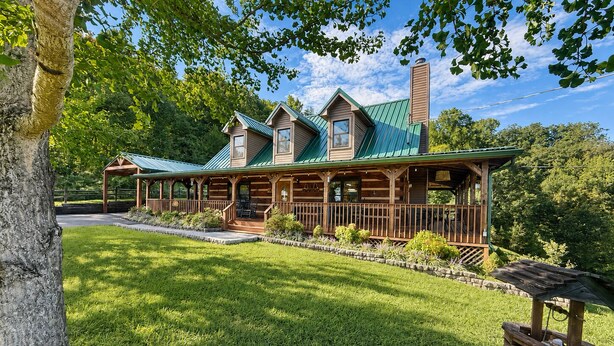 A log cabin with a porch, a chimney, and a well-maintained lawn. - Dogwood Acre 3 Bedroom Cabin by RedAwning (Sevierville)