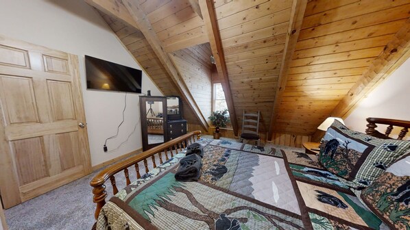 A bedroom with a sloped ceiling, a wooden door, a bed with a patterned bedspread, a dresser, and a mirror.