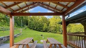 A covered picnic area with two wooden picnic tables and a view of a grassy landscape with trees. - Dogwood Acre 3 Bedroom Cabin by RedAwning (Sevierville)