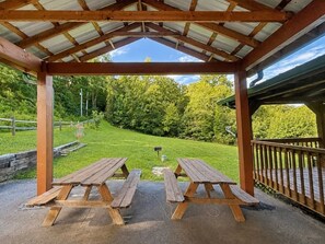 A covered picnic area with two wooden picnic tables and a view of a grassy landscape with trees. - Dogwood Acre 3 Bedroom Cabin by RedAwning (Sevierville)