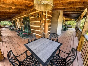 A covered outdoor area with a wooden deck, a table with chairs, and a hanging light fixture. - Dogwood Acre 3 Bedroom Cabin by RedAwning (Sevierville)
