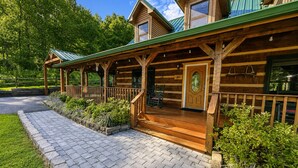 A wooden cabin with a porch, a covered outdoor seating area, and a stone pathway leading to the entrance. - Dogwood Acre 3 Bedroom Cabin by RedAwning (Sevierville)